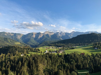 Blick auf die Gemeinde inmitten von grünen Hügeln, Wald und Bergen im Hintergrund